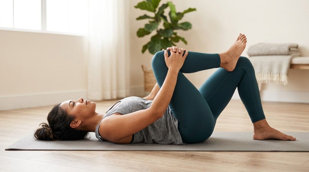 Person performing a supine piriformis stretch by pulling one knee toward the chest while lying on a mat.